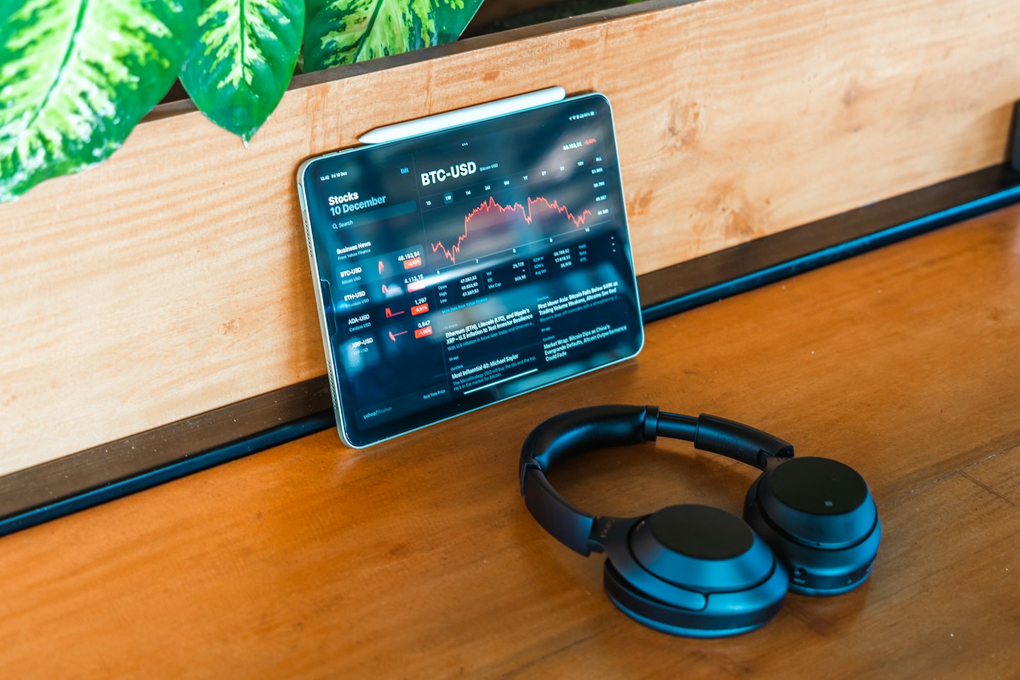 Tablet mit Krypto-Charts, Kopfhörern und Pflanze.